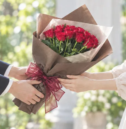 ブラウンのペーパーで包んだ赤いバラの花束を手渡すふたりの手元