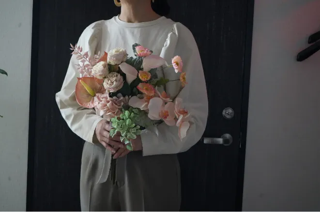 ピンクと白を基調にした花束を両手で抱える人